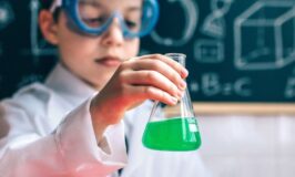 Παιδί με προστατευτικά γυαλιά κρατά μια φιάλη με πράσινο υγρό σε εύκολο πείραμα για παιδιά στο σπίτι